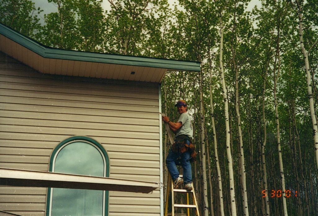 Man posing on ladder while putting up steel siding on house